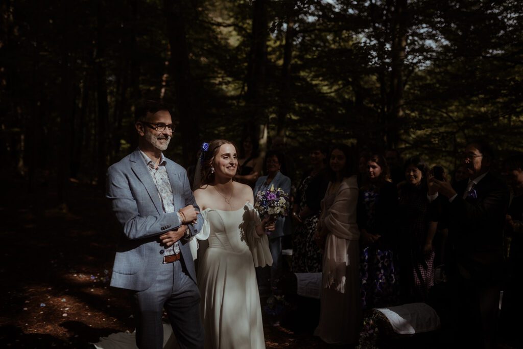 Natürlicher Moment der Hochzeitsgäste beim Einzug, moody artsy Stil, Waldhochzeit Edelstauden